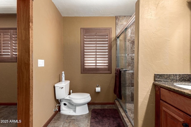 bathroom featuring a textured wall, toilet, a stall shower, vanity, and baseboards