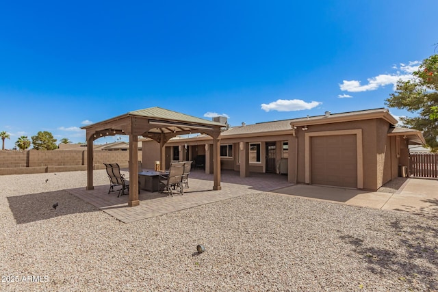 rear view of property with a garage, fence, a gazebo, stucco siding, and a patio area