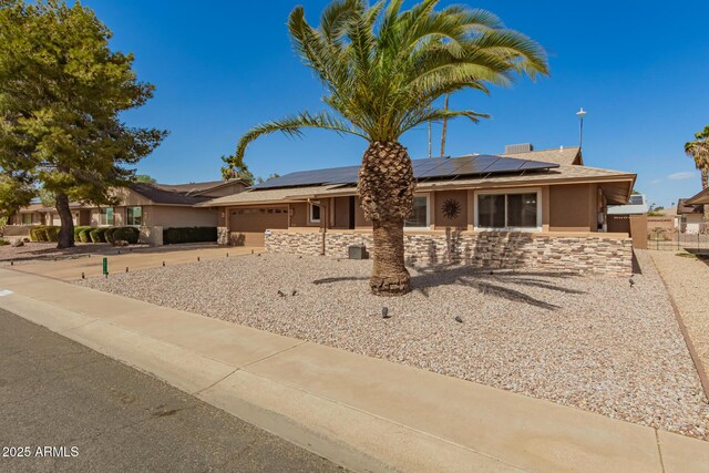 ranch-style home featuring stucco siding, concrete driveway, roof mounted solar panels, a garage, and stone siding