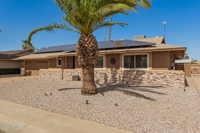 ranch-style house with an attached garage, stone siding, driveway, roof mounted solar panels, and stucco siding