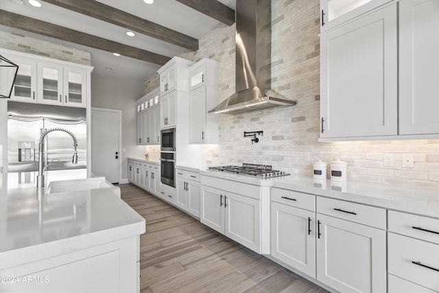 kitchen featuring light wood-type flooring, wall chimney exhaust hood, beam ceiling, sink, and white cabinetry