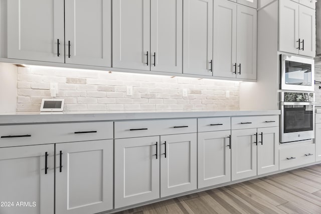 kitchen with light wood-type flooring, stainless steel oven, built in microwave, decorative backsplash, and white cabinetry