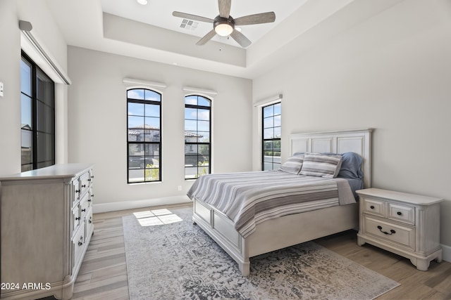 bedroom featuring ceiling fan, a tray ceiling, and light hardwood / wood-style floors