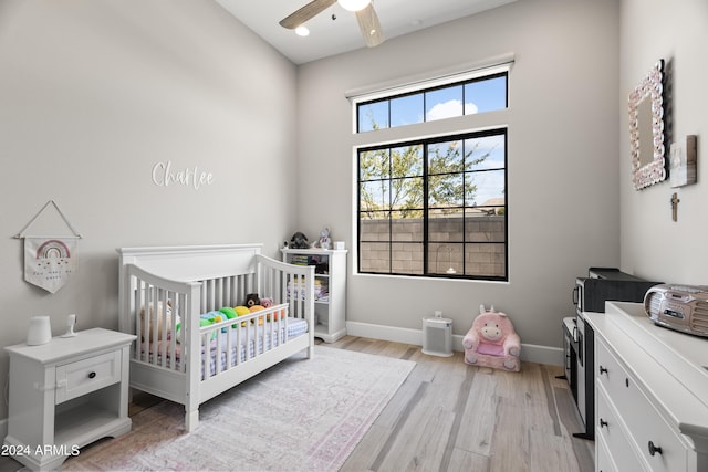 bedroom featuring ceiling fan, multiple windows, light wood-type flooring, and a crib