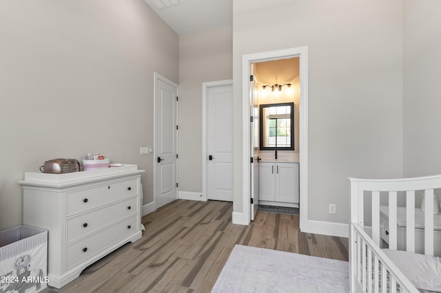 bedroom featuring a nursery area, ensuite bathroom, and light hardwood / wood-style floors