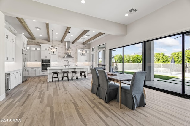 dining room with sink, beverage cooler, beamed ceiling, and light hardwood / wood-style flooring