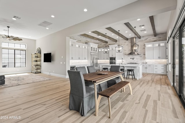 dining space with ceiling fan, light hardwood / wood-style flooring, beamed ceiling, and sink