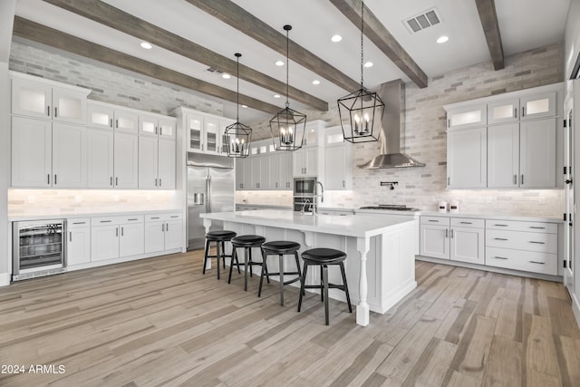 kitchen with built in appliances, wine cooler, wall chimney range hood, and white cabinetry