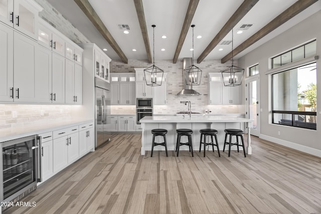 kitchen with built in appliances, white cabinetry, wine cooler, and beam ceiling