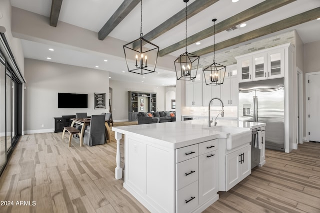 kitchen featuring decorative light fixtures, white cabinetry, beam ceiling, and an island with sink