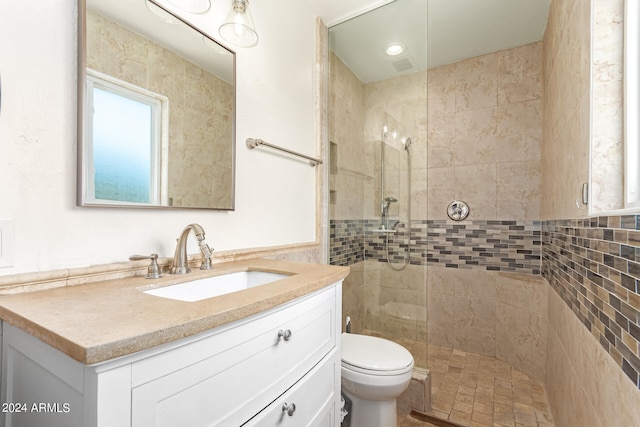 bathroom featuring tiled shower, vanity, toilet, and tile walls