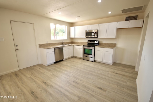 kitchen with appliances with stainless steel finishes, sink, light hardwood / wood-style flooring, and white cabinets