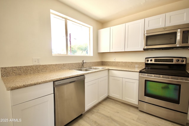 kitchen featuring appliances with stainless steel finishes, sink, white cabinets, and light hardwood / wood-style flooring