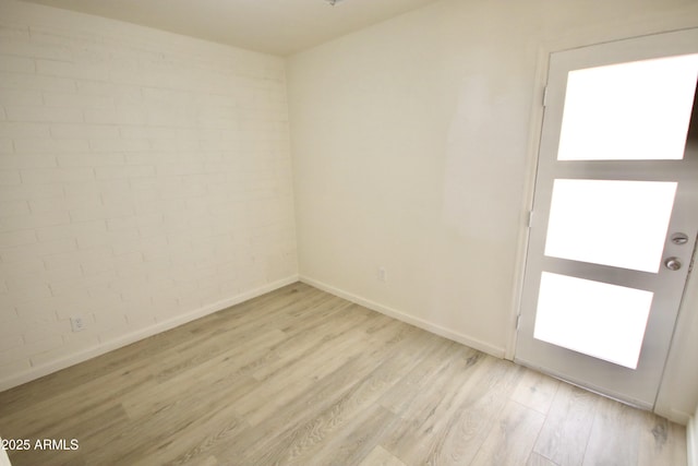 spare room featuring a healthy amount of sunlight, brick wall, and light wood-type flooring