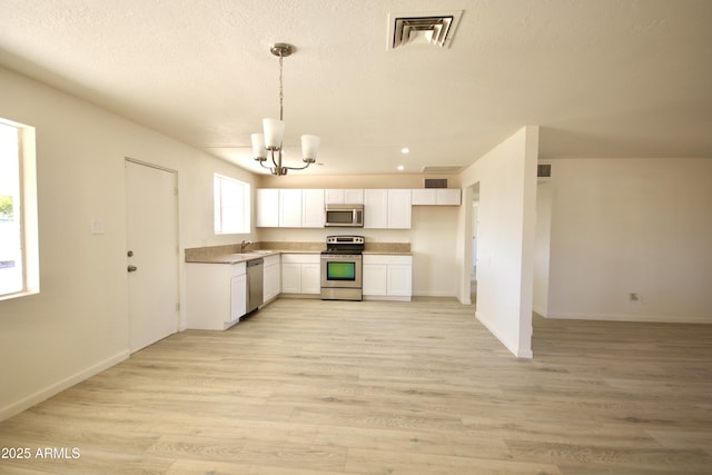 kitchen with appliances with stainless steel finishes, sink, white cabinets, and decorative light fixtures