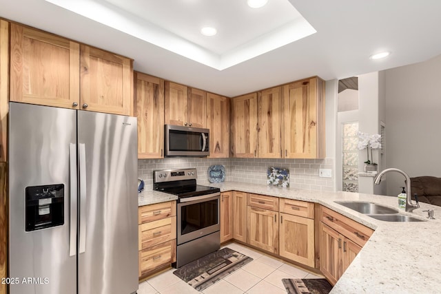 kitchen featuring light tile patterned flooring, a sink, appliances with stainless steel finishes, tasteful backsplash, and a raised ceiling