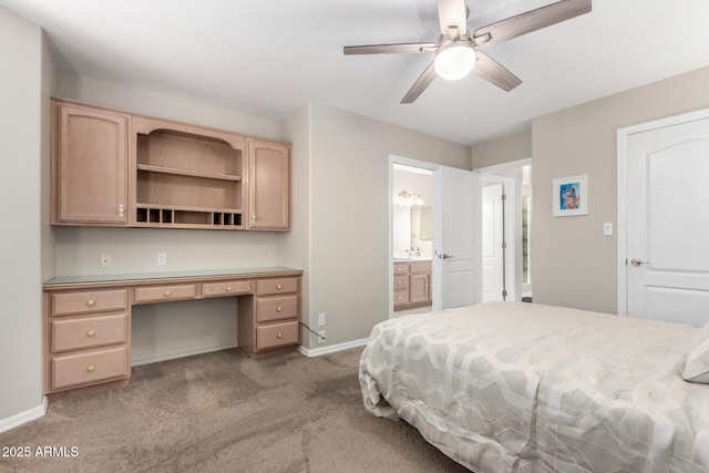 bedroom featuring light colored carpet, built in study area, connected bathroom, ceiling fan, and baseboards