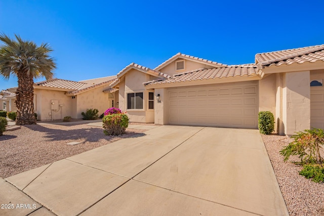 mediterranean / spanish-style house with a garage, driveway, a tiled roof, and stucco siding