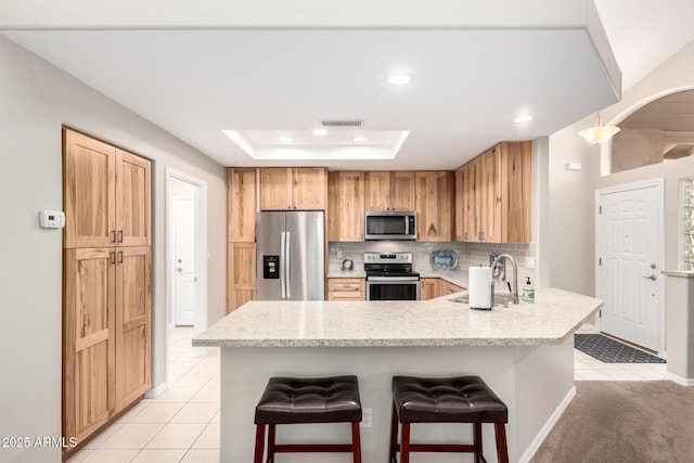 kitchen featuring a tray ceiling, stainless steel appliances, tasteful backsplash, a sink, and a kitchen breakfast bar