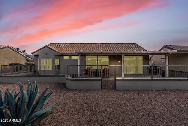 back of house featuring a tile roof, a patio, and stucco siding