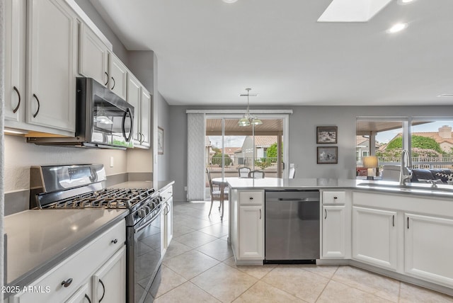 kitchen with light tile patterned flooring, a skylight, a sink, white cabinets, and appliances with stainless steel finishes