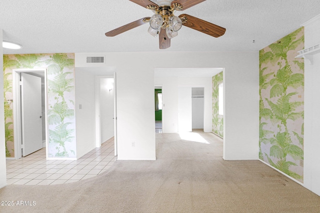 carpeted empty room featuring tile patterned floors, visible vents, a textured ceiling, and wallpapered walls