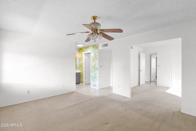 unfurnished room featuring visible vents, light colored carpet, a textured ceiling, and a ceiling fan