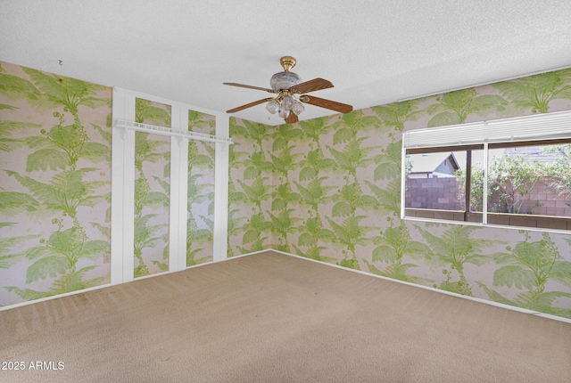 carpeted empty room featuring baseboards, a textured ceiling, wallpapered walls, and a ceiling fan