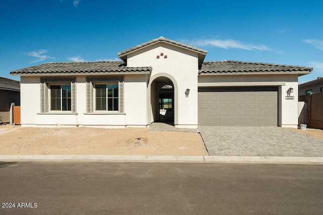 mediterranean / spanish-style home featuring a tiled roof, stucco siding, driveway, and a garage