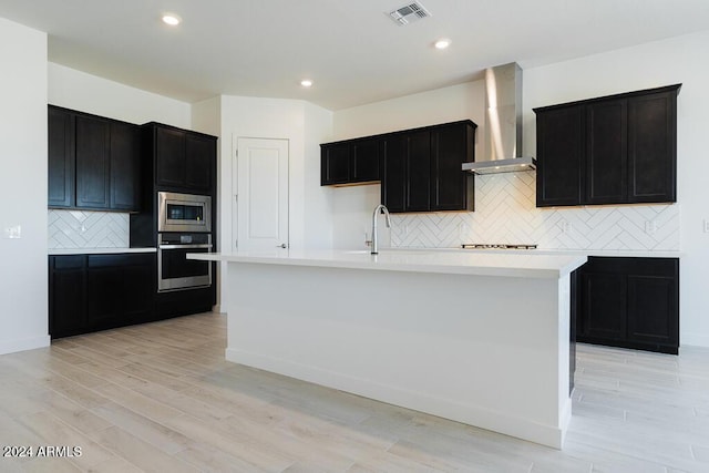 kitchen with wall chimney range hood, visible vents, appliances with stainless steel finishes, tasteful backsplash, and a sink