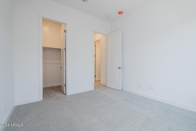 unfurnished bedroom with light carpet, a closet, and a spacious closet