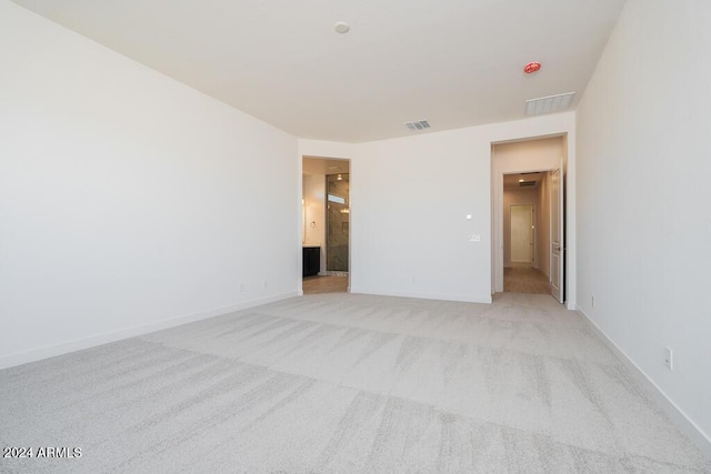 unfurnished bedroom with baseboards, light colored carpet, ensuite bath, and visible vents