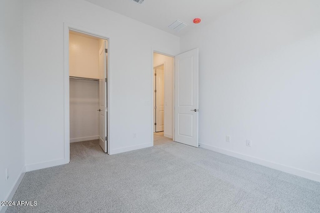 unfurnished bedroom with baseboards, carpet, a walk in closet, and visible vents