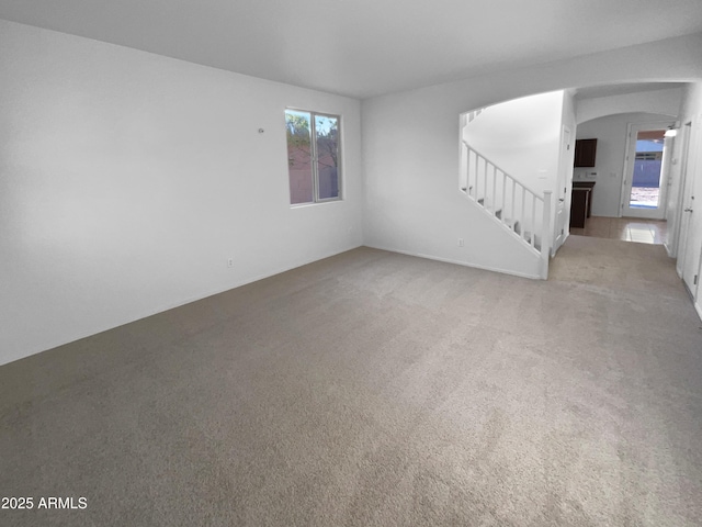 empty room featuring arched walkways, carpet flooring, and stairs