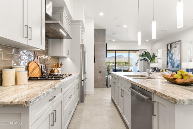 kitchen with an island with sink, hanging light fixtures, wall chimney exhaust hood, and stainless steel appliances