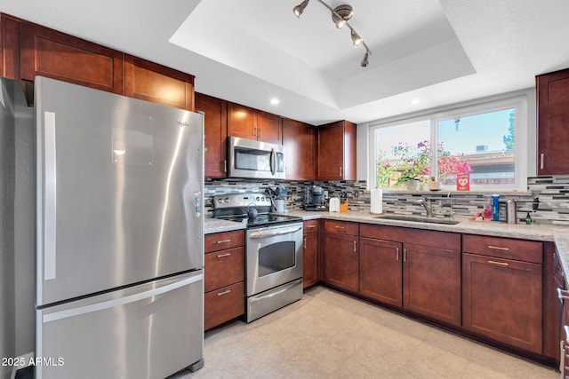 kitchen featuring a sink, a tray ceiling, backsplash, stainless steel appliances, and light stone countertops