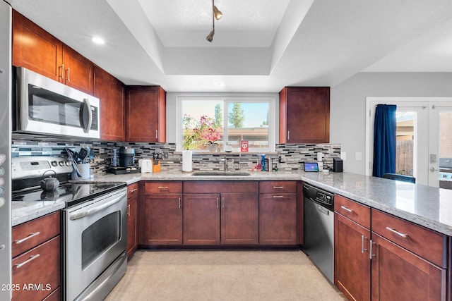 kitchen with light stone counters, stainless steel appliances, a raised ceiling, and a sink