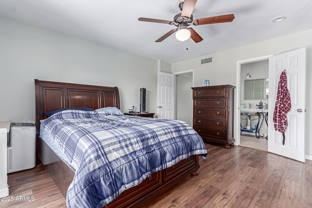 bedroom featuring a ceiling fan, visible vents, ensuite bath, and wood finished floors