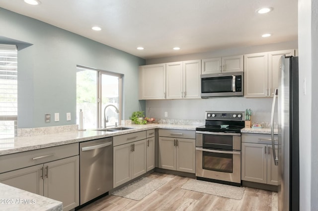 kitchen with gray cabinets, sink, light stone counters, light hardwood / wood-style floors, and stainless steel appliances