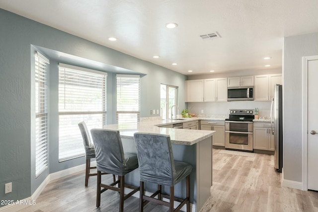 kitchen featuring sink, appliances with stainless steel finishes, a kitchen bar, kitchen peninsula, and light wood-type flooring