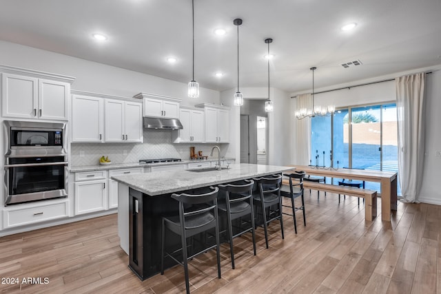 kitchen featuring hanging light fixtures, stainless steel appliances, light hardwood / wood-style flooring, an island with sink, and white cabinets