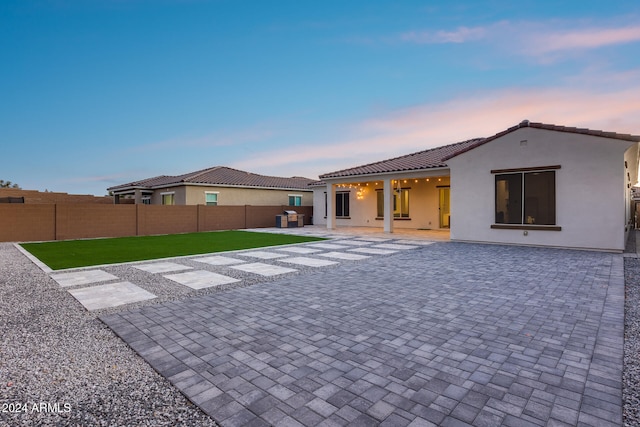 back house at dusk featuring a yard and a patio