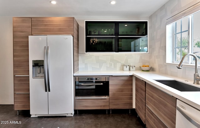 kitchen featuring dishwasher, fridge with ice dispenser, brown cabinetry, and a sink