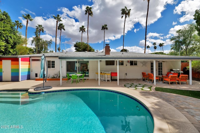 back of house featuring an outdoor pool, outdoor lounge area, a chimney, and a patio area