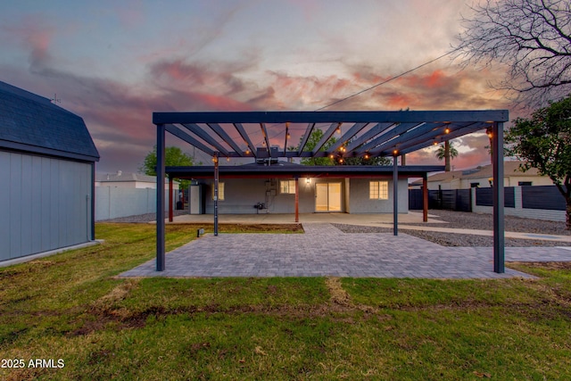 back of property at dusk featuring an outbuilding, fence, a yard, a pergola, and a patio area