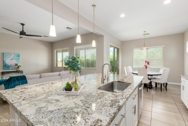 kitchen with light stone countertops, white cabinetry, sink, and a kitchen island with sink