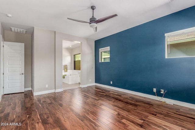 unfurnished bedroom featuring dark hardwood / wood-style floors, ensuite bath, multiple windows, and ceiling fan