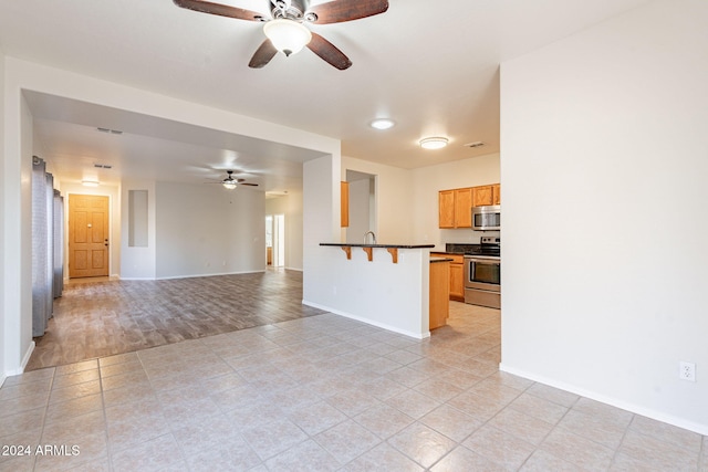 kitchen with appliances with stainless steel finishes, ceiling fan, a breakfast bar area, and light tile patterned floors