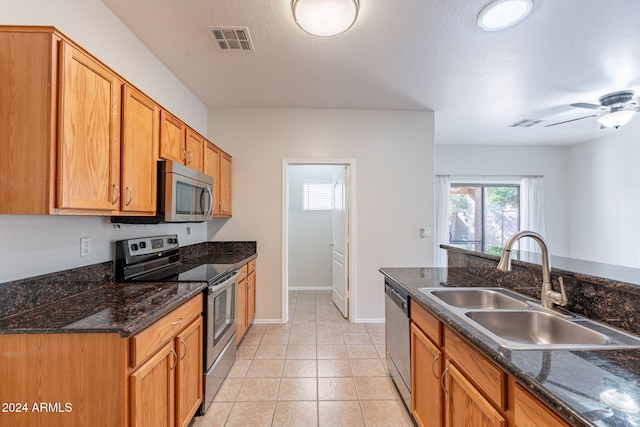 kitchen featuring appliances with stainless steel finishes, ceiling fan, dark stone countertops, and sink