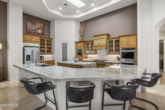 kitchen with a high ceiling, a skylight, appliances with stainless steel finishes, a large island, and a kitchen bar